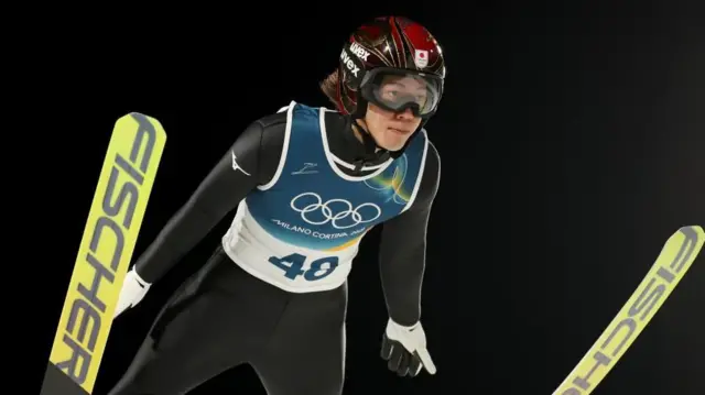 二階堂が空中で両手とスキーを開き、前傾姿勢を取っている