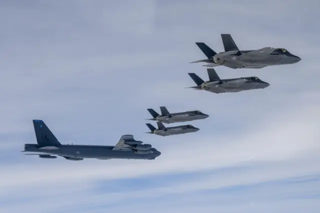 A US Air Force B-52H strategic bomber (L) flying with South Korean Air Force F-35A fighter jets during a joint air drill on 14 April 