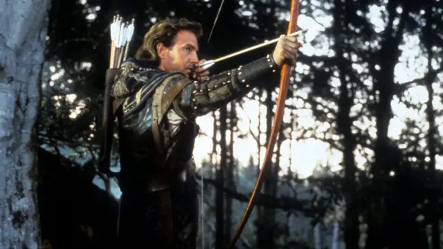 Kevin Costner, elinde ok ve yay ile ormanda Robin Hood rolünde
