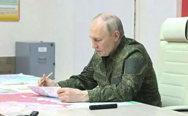 Rusya Devlet Başkanı Vladimir Putin, askeri üniformasıyla oturuyor ve haritaları inceliyor. Tek başına görünüyor.