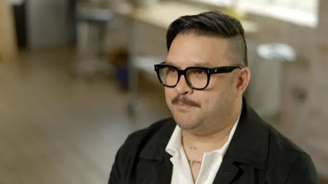 ویل هیوارد، مردی با عینک‌های قاب مشکی، سبیلی باریک و موی قهوه‌ای تیره که سمت چپ سرش نزدیک به پوست تراشیده شده و به سمت دیگر شانه شده است. او کت تیره و پیراهن سفیدی با یقه باز به تن دارد.