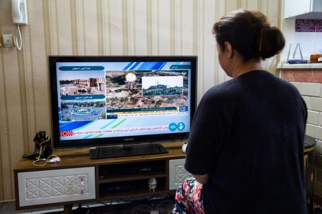 زنی در خانه گزارش حمله روز جمعه ۳۱ فروردین در تلویزیون ایران را تماشا می‌کند