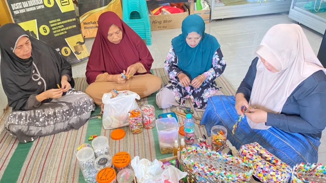 Bersama sejumlah perempuan di desanya, Dwi menganyam tas belanja berbahan sampah plastik yang telah dipotong-potong. 