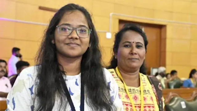 Samyuktha (à gauche) et sa mère Amuthavalli debout l'une à côté de l'autre dans une salle - à l'arrière-plan, de nombreuses autres personnes sont assises