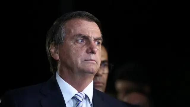 Fotografia colorida mostra Jair Bolsonaro com um terno pretojogo do dado na betanofrente a um fundo escuro