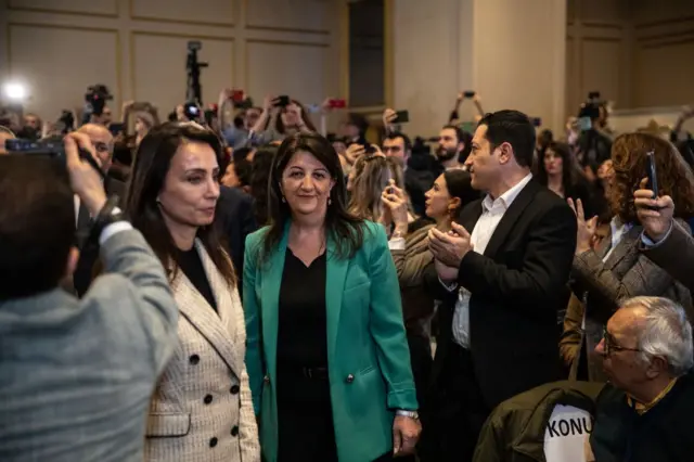 Odakta Pervin Buldan yeşil ceketiyle alkış tutan kalabalığın içinden geçiyor.