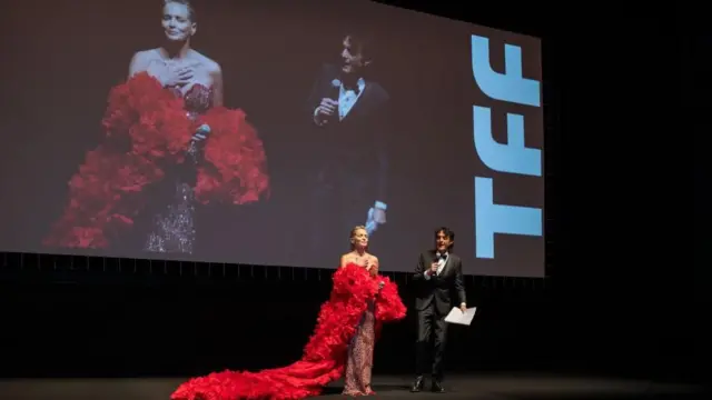 Sharon Stone con un vestido con una larga cola roja, hablando frente a una pantalla que la muestra, en el Festival de Cine de Turín, noviembre de 2024