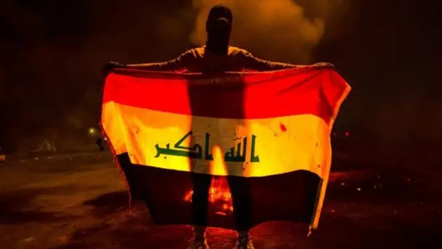 متظاهر ملثم يحمل علم العراق