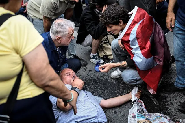 Yerde yatan bir adam, yanında Türk bayrağına sarınmış bir genç