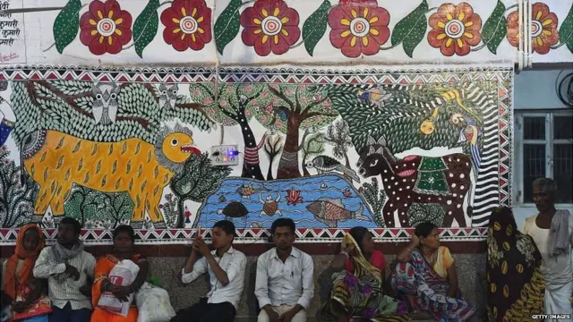 April 7, 2018, shows Indian passengers waiting for train in a area decorated with Mithila or Madhubani paintings at Madhubani railway station in Madhubani, Bihar state.