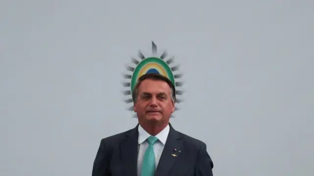 Bolsonaro em pé em frente a painel com símbolo brasileiro