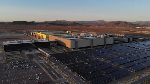 Um prédio de fábrica, ao lado de painéis solares, no meio do deserto