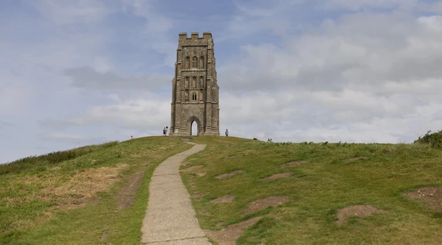 언덕 위에 돌로 지은 탑이 서 있고, 탑 주변으로 사람들이 걷고 있다.