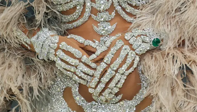 Zbliżenie na bogato zdobioną część stroju Beyoncé: jasny gorset pokryty gęstymi, błyszczącymi ozdobami przypominający żebra i elementy szkieletu. Po bokach widoczne są puszyste pióra w jasnoszarym odcieniu.