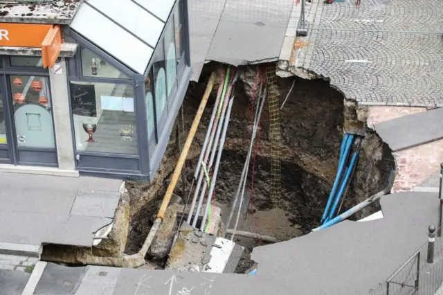 TOPSHOT - Construction workers stand near a sinkhole along a street in the city of Amiens, northern France, on August 13, 2019. - A five metres deep and ten metres wide sinkhole appeared in the centre of Amiens overnight on August 11, which the local municipal services believe could have been triggered by the collapse of a medieval cave in the vicinity. (Photo by DENIS CHARLET / AFP) (Photo by DENIS CHARLET/AFP via Getty Images)