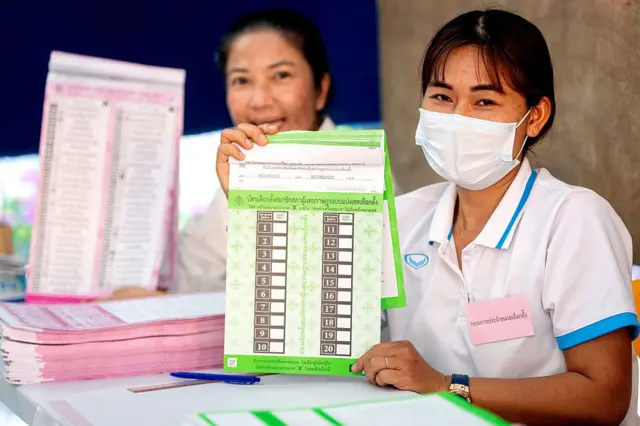 ထိုင်းရွေးကောက်ပွဲမှာ ထည့်ရမယ့် အစိမ်းရောင်နဲ့ ပန်းရောင်မဲစာရွက်တွေကို ပြသနေတဲ့ ထိုင်းမဲရုံလုပ်သား ၂ ဦး 