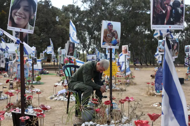 Um homem sentadomrjack. betuma cadeira no memorial onde ocorreu o festivalmrjack. betmúsica — ele está cercado por bandeiras israelenses e fotosmrjack. betpessoas que foram mortas no ataque.