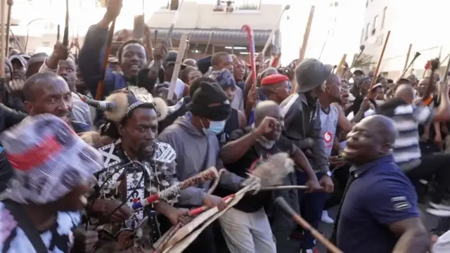 Anti-migrant protesters for South Africa - mainly men hold sticks, one of dem dey dressed in Zulu traditional clothing.