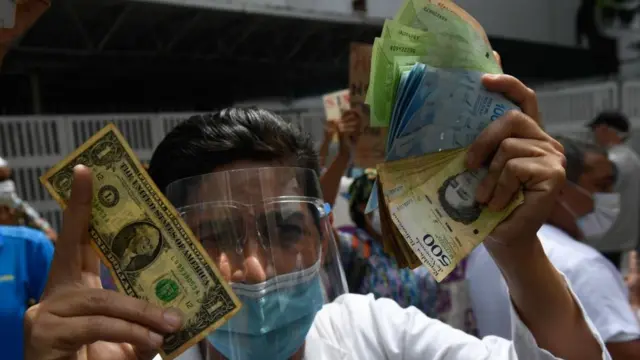 Un hombre sostiene un dólar y un puño de bolívares