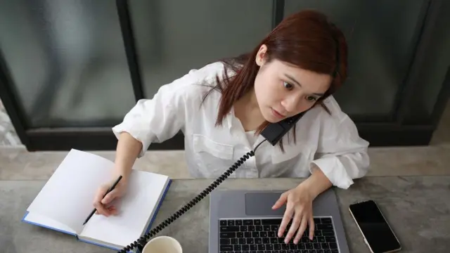 Mulher falando ao telefone enquanto digita no laptop