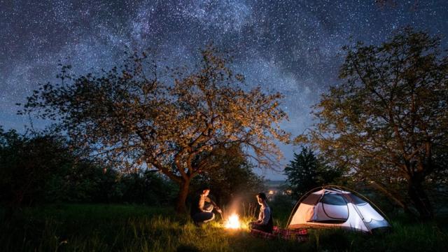Un couple de campeurs, assis près d'un feu de camp, avec un ciel étoilé au-dessus d'eux.