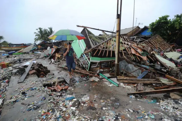 TOPSHOT - Seorang pria berjalan melewati puing-puing di desa Teluk, Kecamatan Labuan, Provinsi Banten pada 26 Desember 2018, setelah tsunami - yang disebabkan oleh aktivitas gunung berapi yang dikenal sebagai "anak" Krakatoa - menghantam pantai barat Pulau Jawa, Indonesia pada 22 Desember.