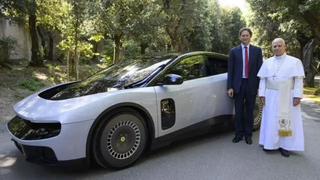 白い車の隣に、白い法服のレオ14世とダークスーツ姿の人が並んで立っている