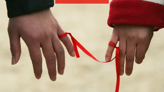 İki el fotoğrafı. Birinin küçük parmağı diğerinin işaret parmağı birbirine kırmızı bir kurdele ile bağlı. 