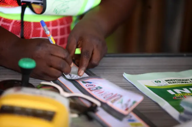 Aworan oṣiṣẹ idibo kan to n kọ iwe lori tabili nibi eto idibo kan.