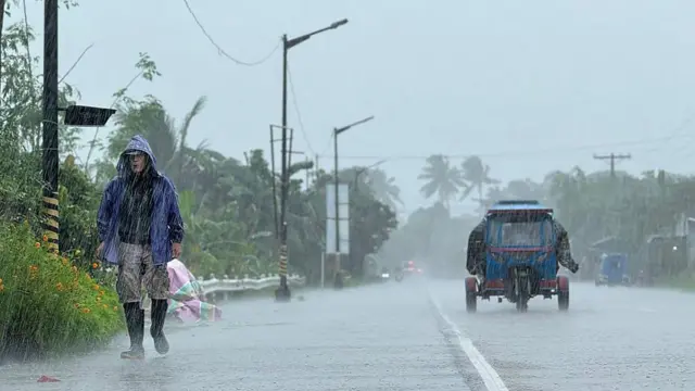 Un hombra camina con botas de agua y un chubasquero bajo lluvias torrenciales.
