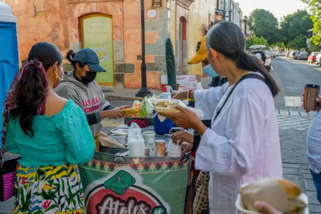 Una vendedora de comida atiende a varios clientes en una calle de México
