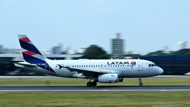 Avião da Latam taxiando na pista do Aeroporto de Congonhas, com a aeronave em movimento e a área urbana ao fundo.