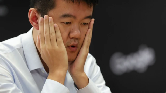 Ding Liren se lleva las manos a la cara después de darse cuenta de su error crucial durante la última partida del Campeonato Mundial de Ajedrez de 2024. Lleva una camiseta blanca.