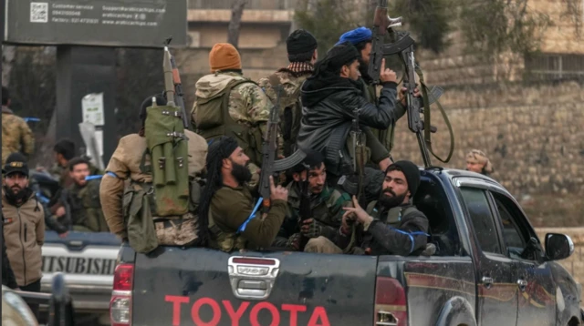 Bir Toyota araacının arkasında en az sekiz kimi ağır silahlı savaşçı görülüyor. Yanlarında başka araçlarda başka silahlı kişiler var.