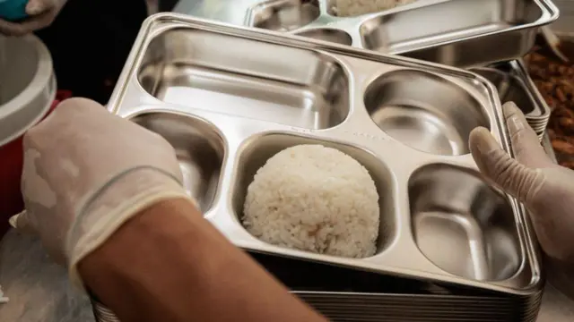 Seorang relawan sedang mempersiapkan makan bergizi gratis ke dalam ompreng.