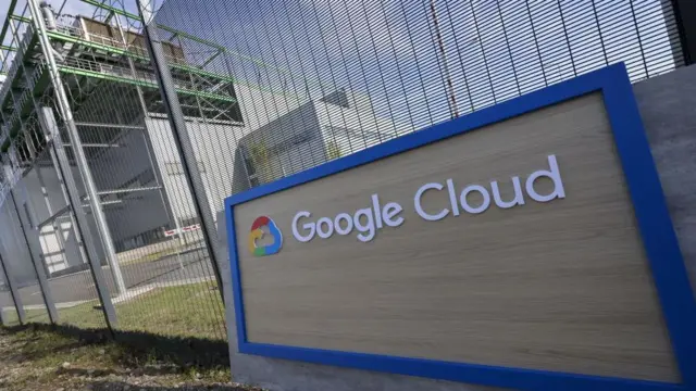 Un cartel de Google Cloud sfrente a una verja. Detrás hay un centro de datos. 
