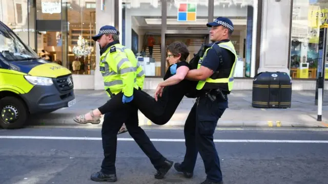 Двое полицейских уносят демонстранта на фоне магазинной витрины