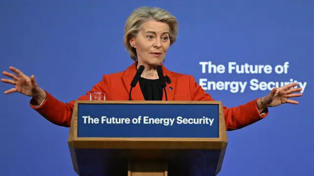 Женщина в красном пиджаке выступает на трибуне