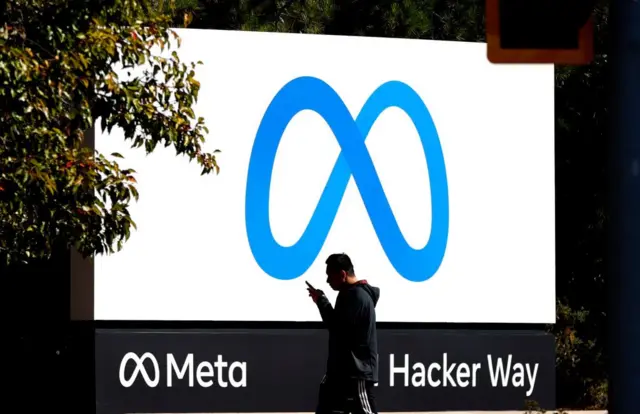 Un peatón camina frente a un nuevo logotipo y el nombre «Meta» en el letrero situado ante la sede de Facebook.