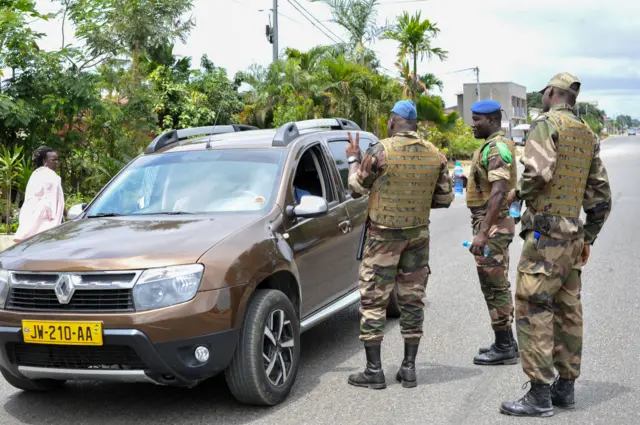 Des membres des forces de sécurité font un geste à un conducteur, à un poste de contrôle dans les rues d'Akanda, au Gabon.