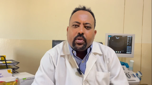 ዶ/ር ሳምሶን ምሉጌታ ወናኒን ኣመሓዳርን ማእከል ሕክምና ኣደታትን ህፃናትን ኣደ፡ ጻዕዳ ጋወን ገይሩ ናብ ካሜራ እናርኣየ