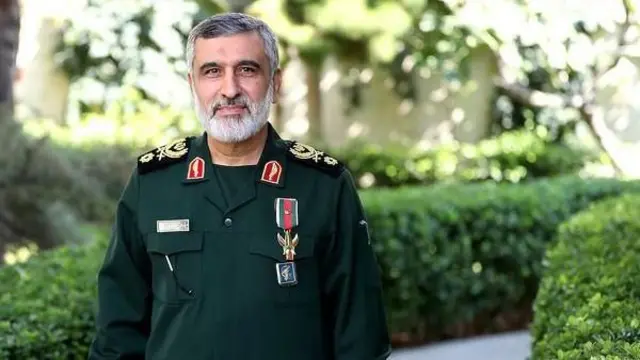 امیرعلی حاجی زاده با لباس نظامی در فضای باز به دوربین نگاه می‌کند