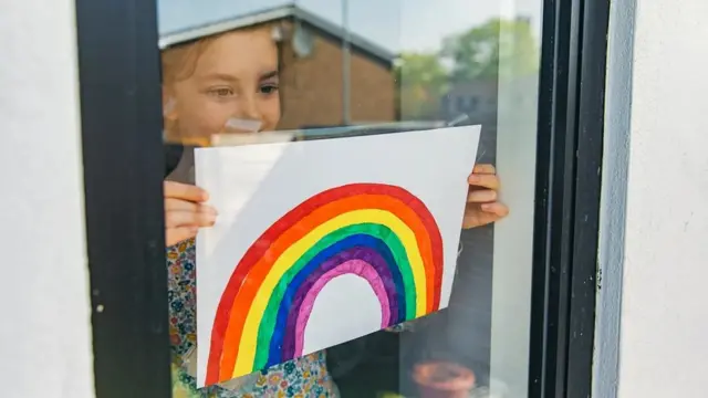 창 안 쪽에서 한 소녀가 무지개 그림을 들고 있는 모습