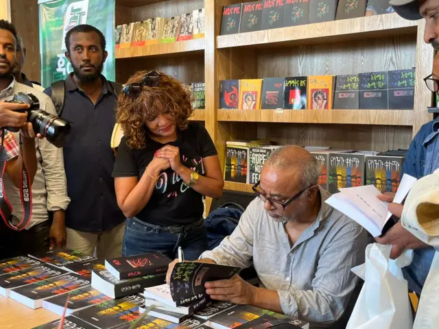 አዳም ረታ ለአንባቢዎቹ መጽሐፉን እየፈረመ