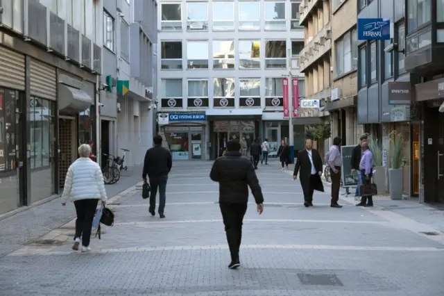 Personas caminando por una calle peatonal rodeada de edificios comerciales en Amberes.