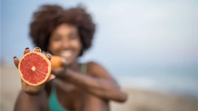 Une femme nous montre une moitié de pamplemousse