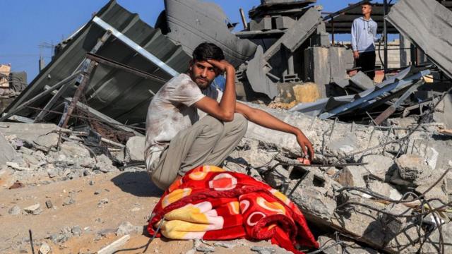 A Palestinian youth sits by the rubble of a building following an Israeli air strike in Rafah in the southern Gaza Strip on October 13, 2023