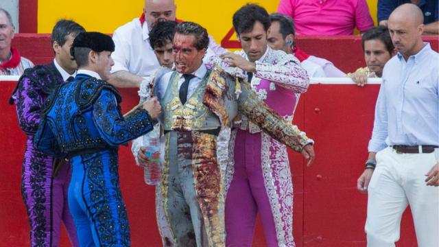 Spanish bullfighter Ivan Fandino (C) covered in the bull"s blood after he was tossed but not gored in a bullfight in the Fiesta de San FermÃ­n in Pamplona, northern Spain, 10 July 2015