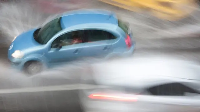 Un auto que parece pasar muy rápido al lado de otro, en una vía llena de agua