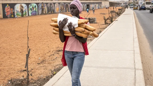 Une jeune femme marche dans la rue en tenant des baguettes de pain